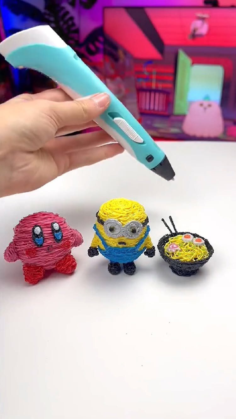 3D printing pen held above small plastic figures of Kirby, a Minion, and ramen.