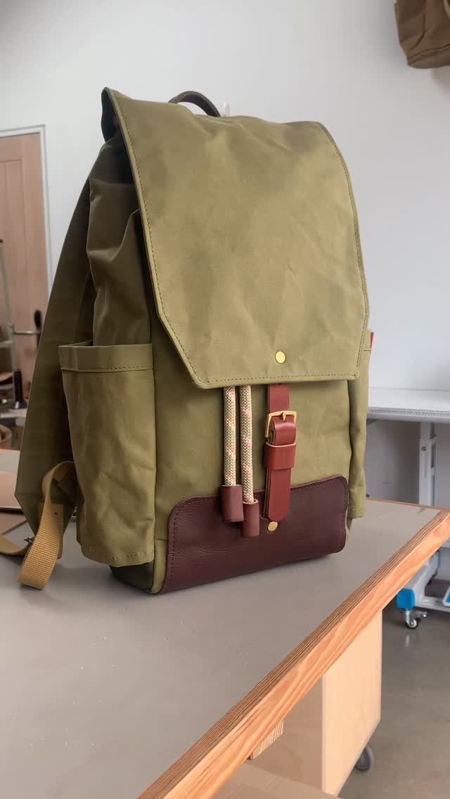 Olive green fabric backpack with brown leather accents resting on a wooden table.