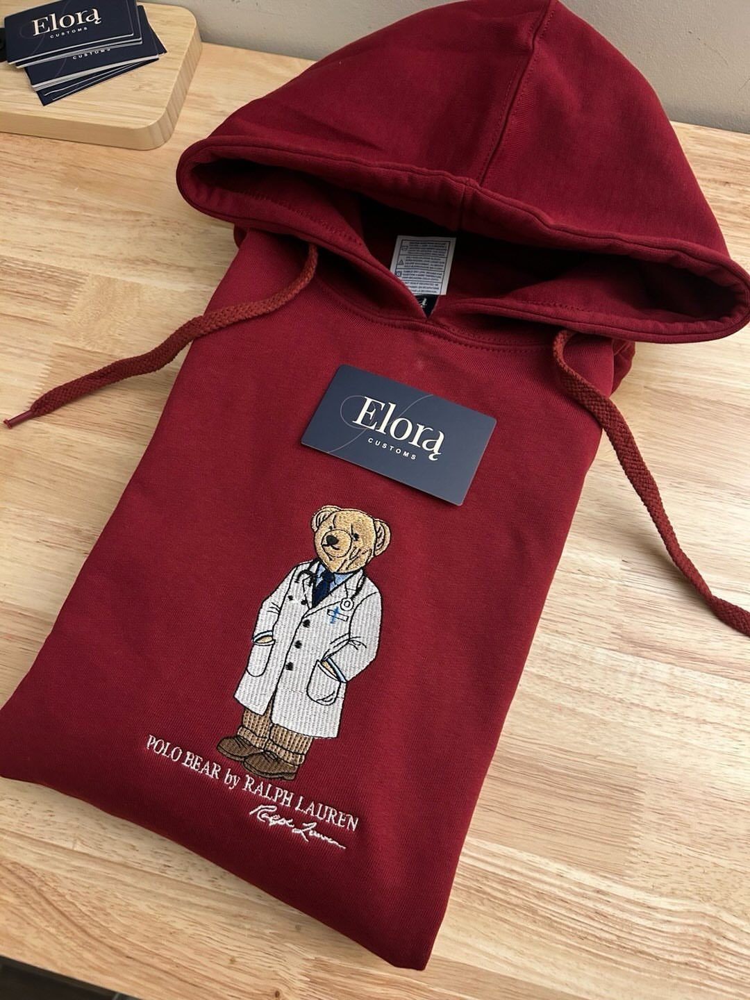 Maroon Ralph Lauren Polo Bear hoodie on a light wooden table surface
