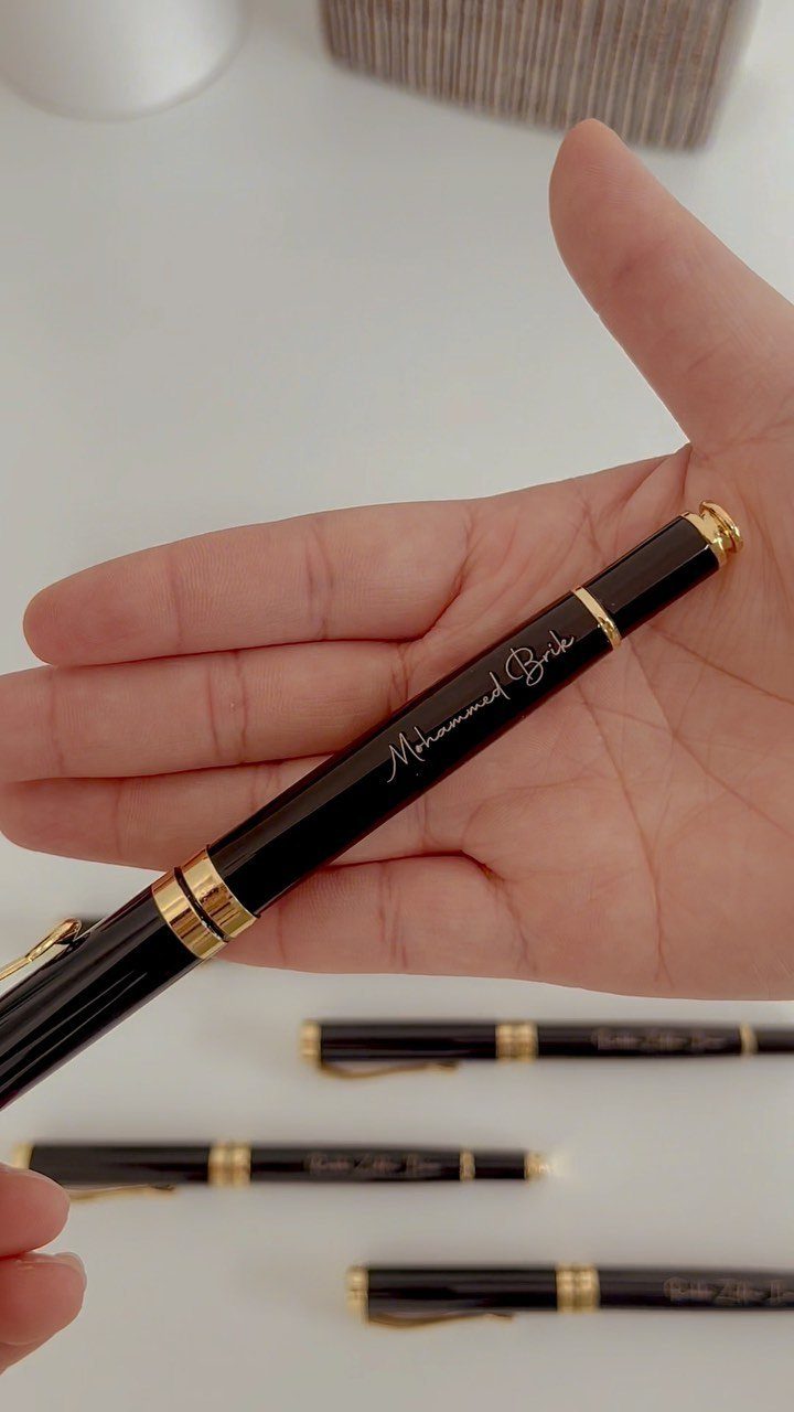 Black and gold engraved pen held in a hand over other pens