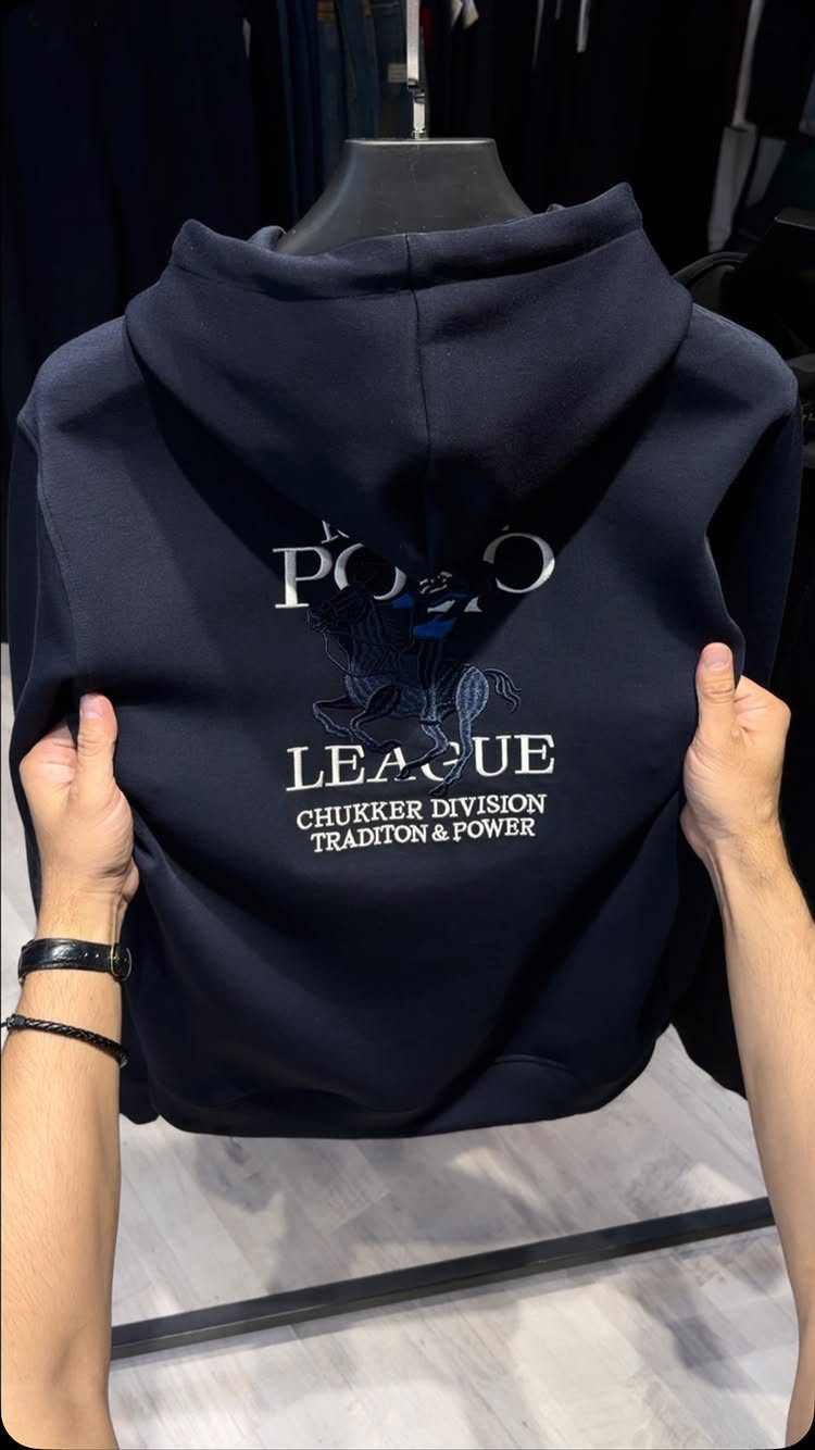 Navy blue Polo League hoodie held up by hands against a store background