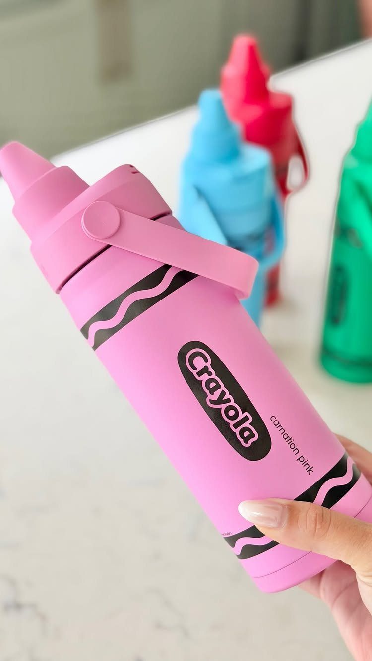 Pink Crayola marker shaped water bottle held by a hand against white background
