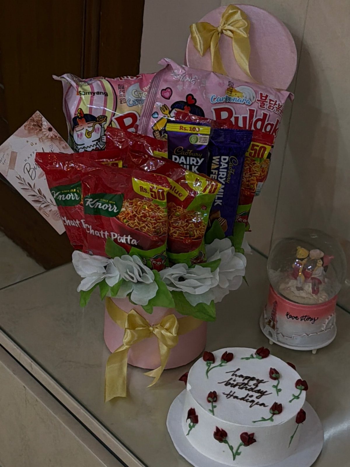 Snack bouquet in a pink box with a small birthday cake and roses.