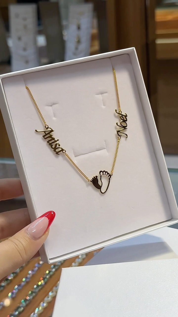 Gold necklace with baby footprint and name charms in a white gift box