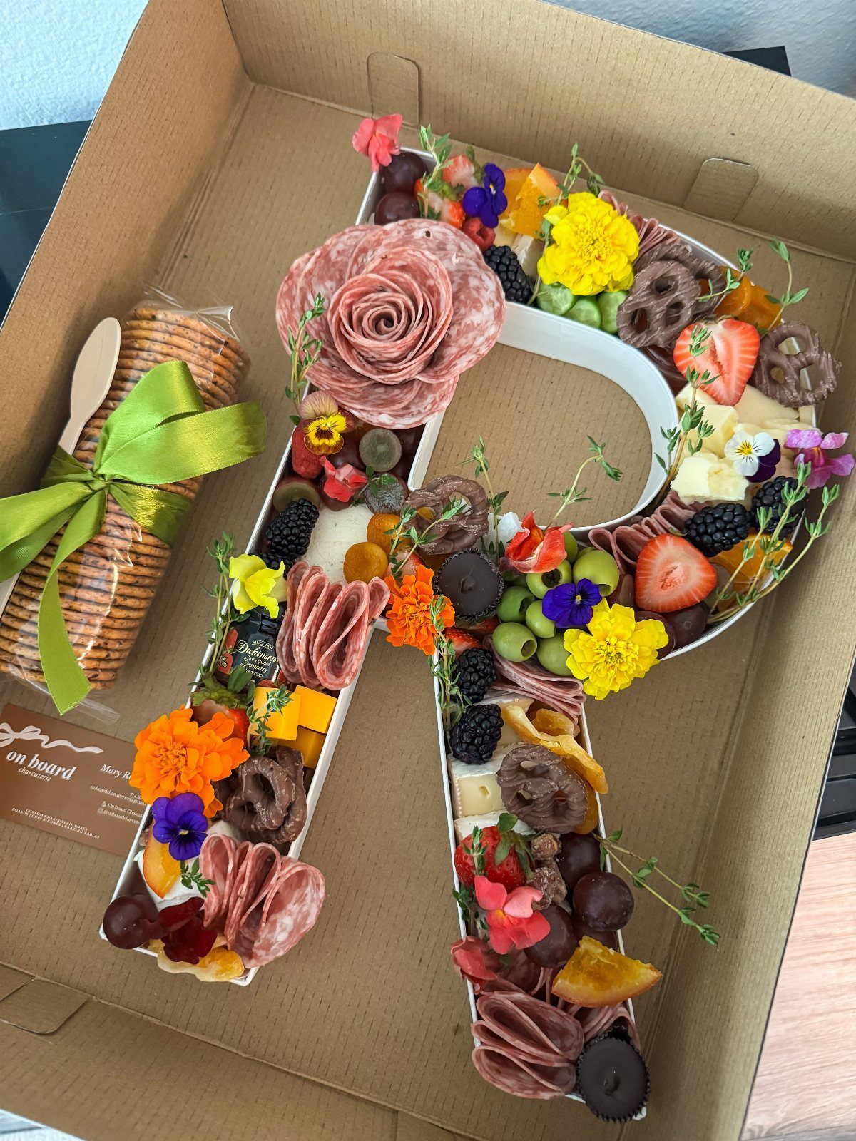 Letter A shaped charcuterie board filled with meats, cheeses, fruits, and edible flowers.