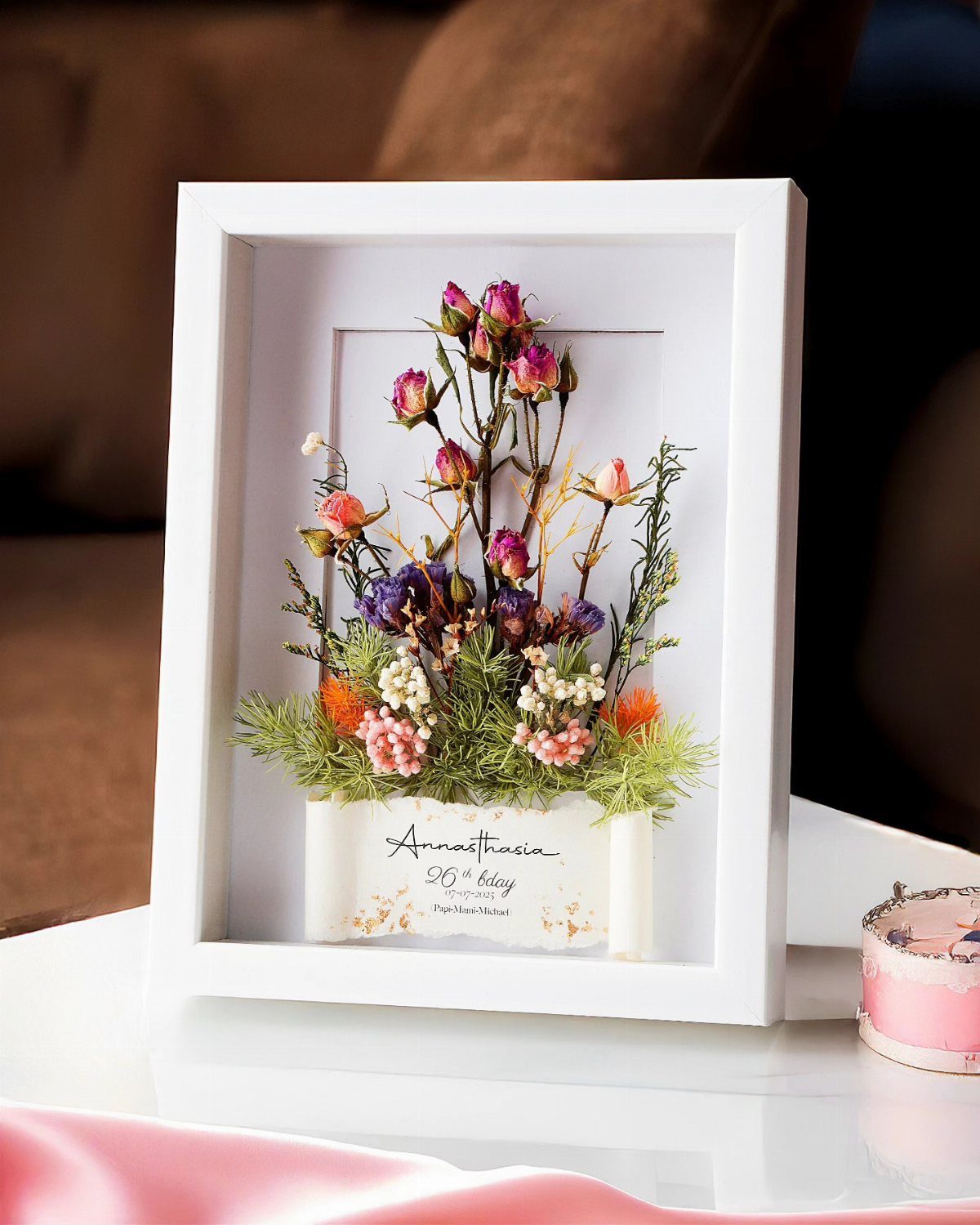 Preserved floral arrangement in a white shadow box frame with a personalized name card.