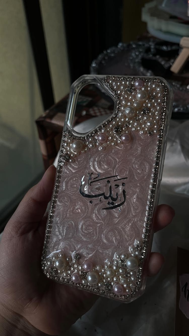 Decorated phone case with pink floral patterns, white pearls, and Arabic calligraphy.