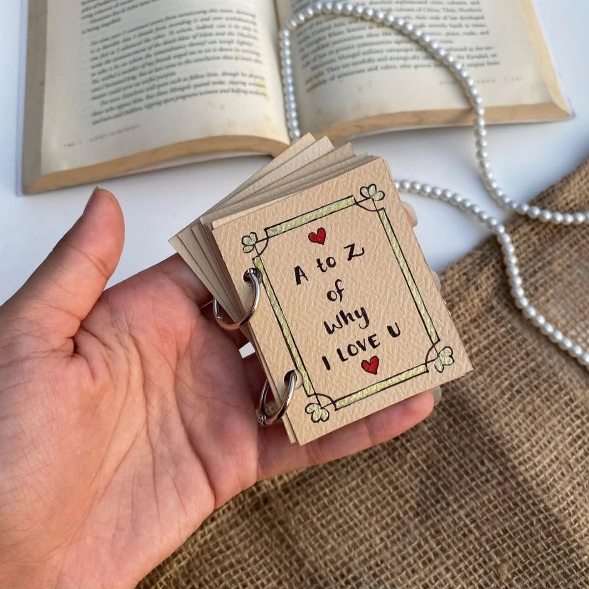 Hand holding a small handmade ring-bound booklet with a romantic handwritten message.