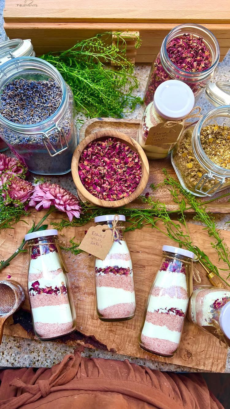 Layered pink and white bath salts in small bottles surrounded by dried petals.