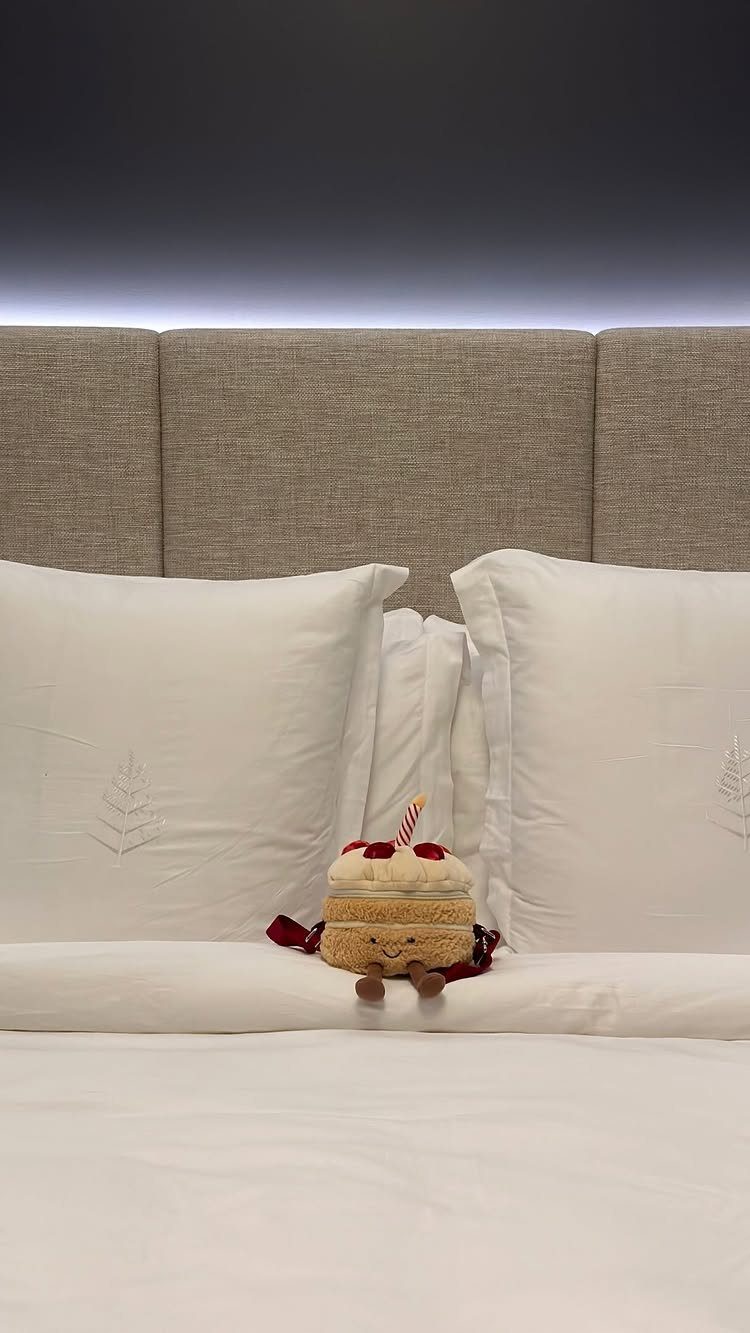Small plush cake toy with a smiling face sitting on white bed linens.
