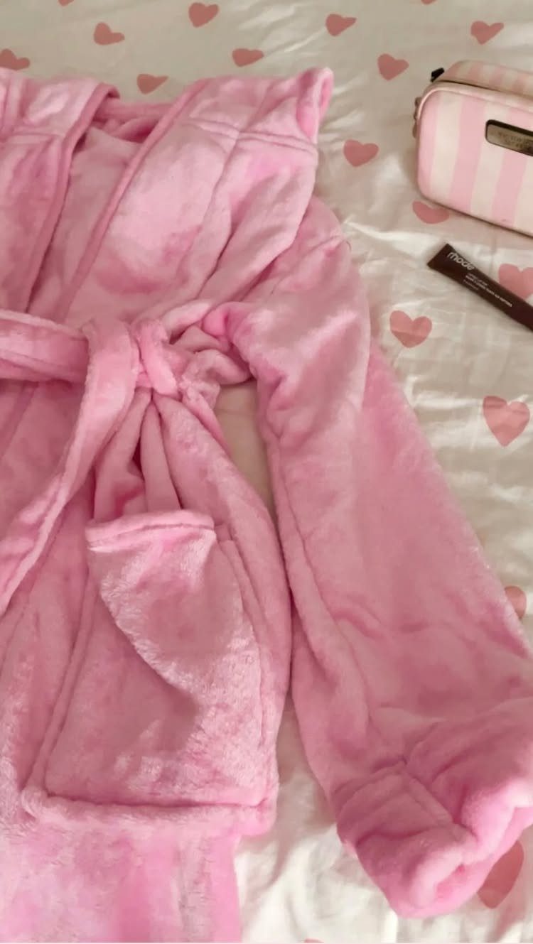 Plush light pink fuzzy robe laid on a heart-patterned white background.
