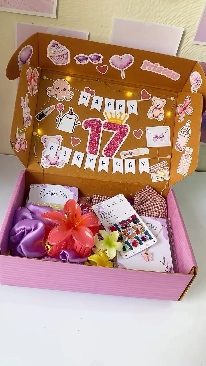 Open pink birthday gift box with hair accessories and decorated inner lid.