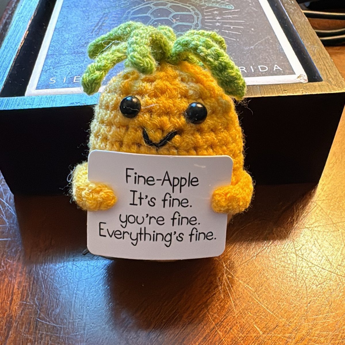 Crocheted pineapple plush holding a sign that says everything is fine.