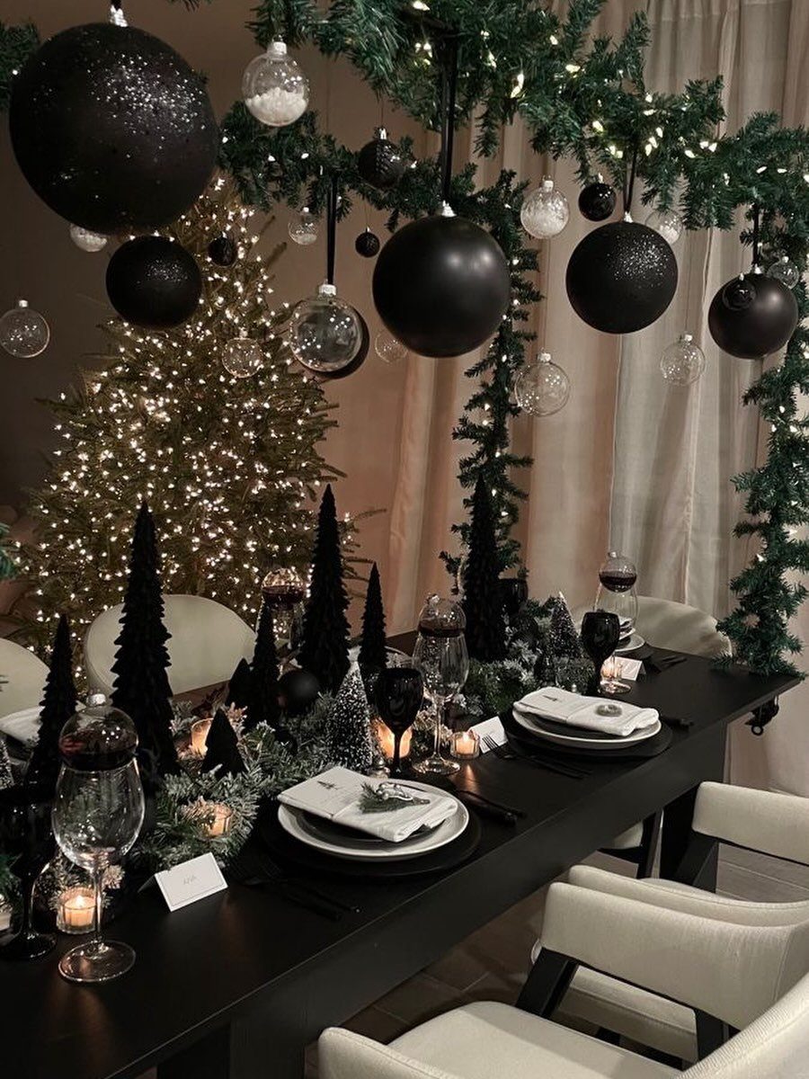 Black dining table set with white plates and black miniature holiday trees.