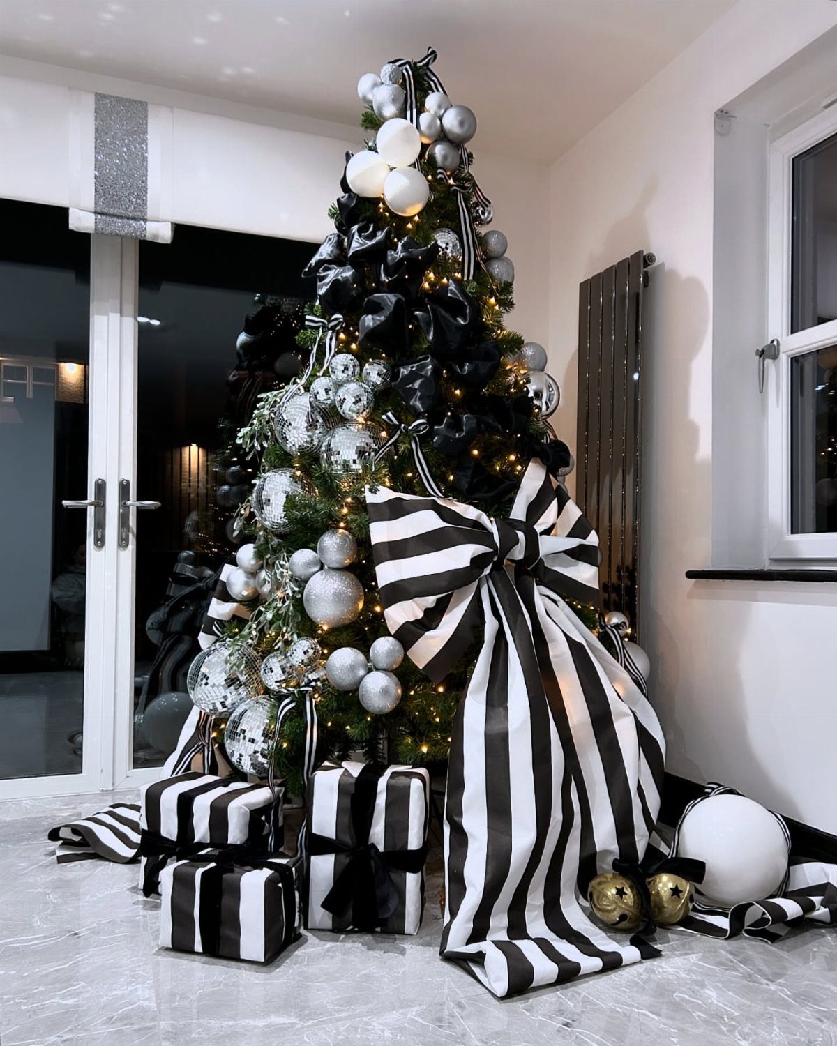 Decorated Christmas tree with black, silver, and white ornaments and striped gift boxes.