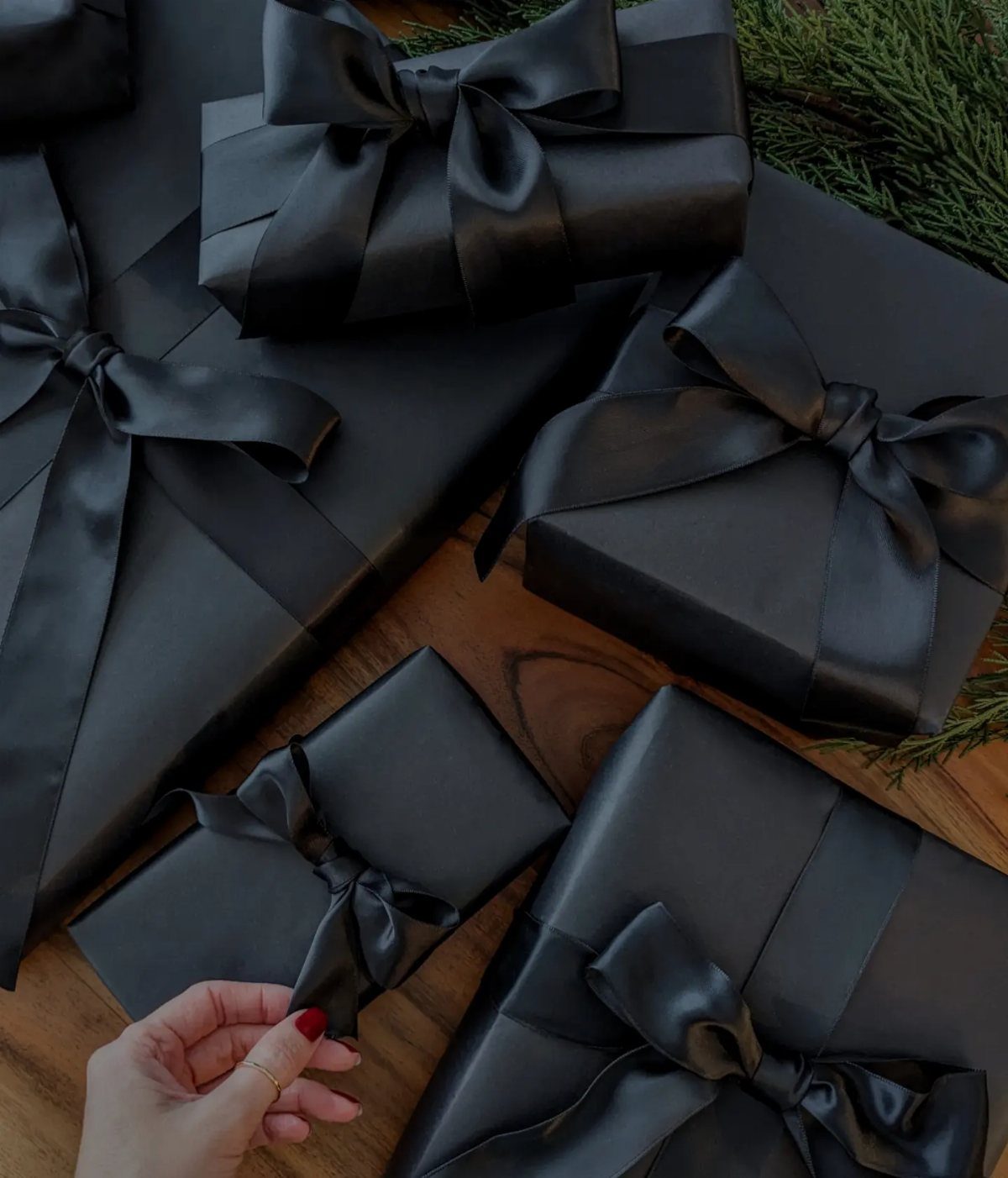 Black wrapped gift boxes with satin ribbons on a wooden table with greenery