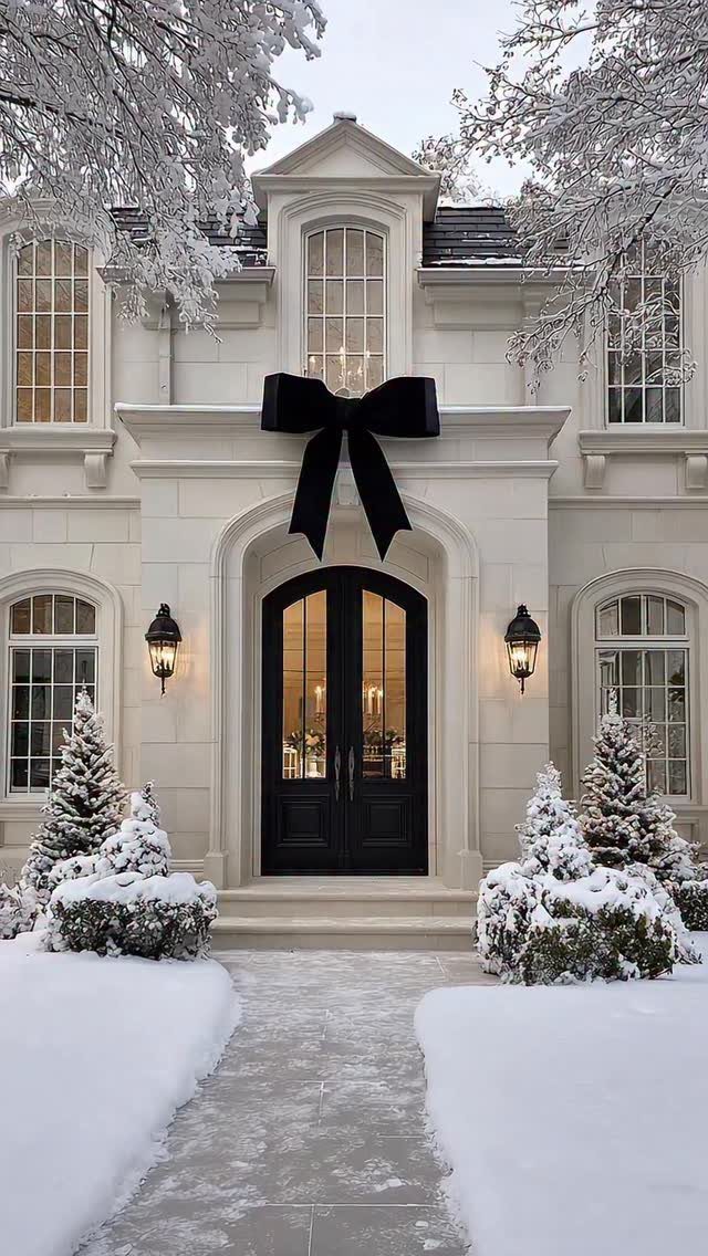 White stone house exterior with a large black bow above black front doors