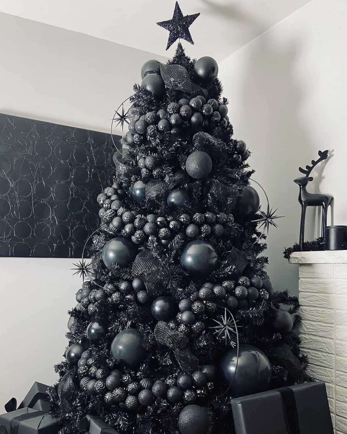 Black Christmas tree decorated with black ornaments and a star topper with black gifts.