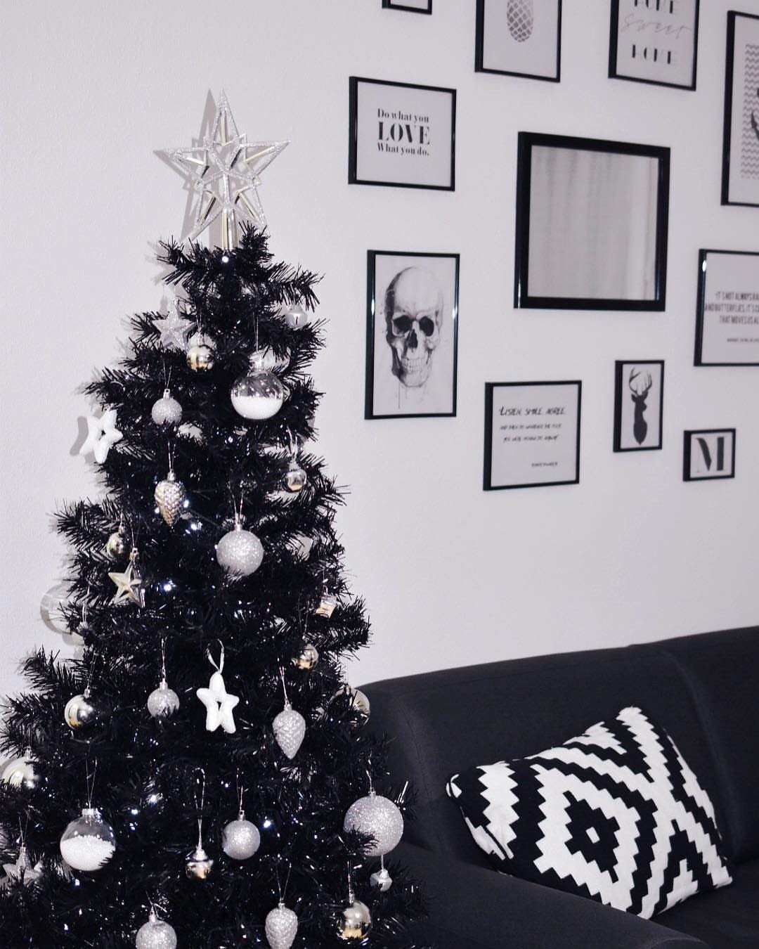 Black Christmas tree with silver ornaments and star topper in a modern room.