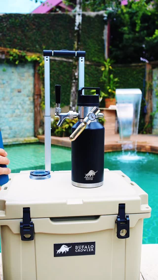 Black insulated beer growler with tap on a beige cooler by a pool