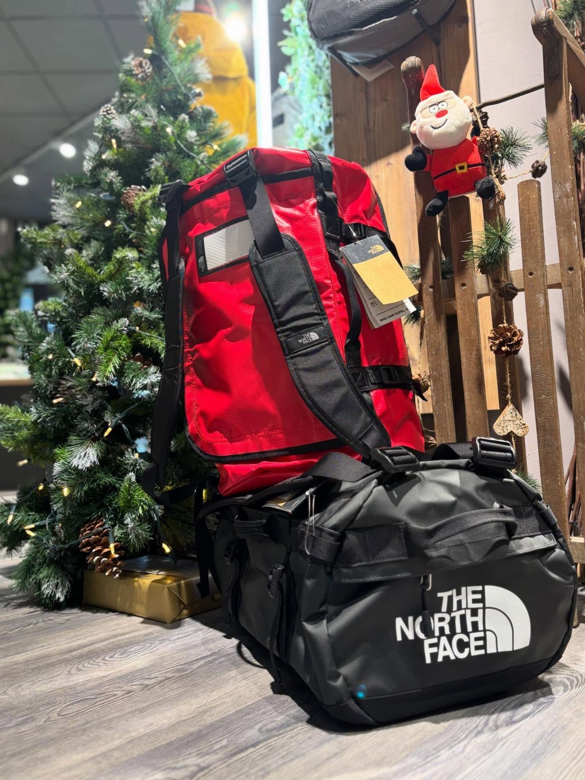 Red and black The North Face duffel bags next to a Christmas tree.