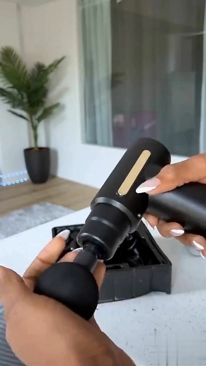 Black handheld massage gun held by hands over a black storage case
