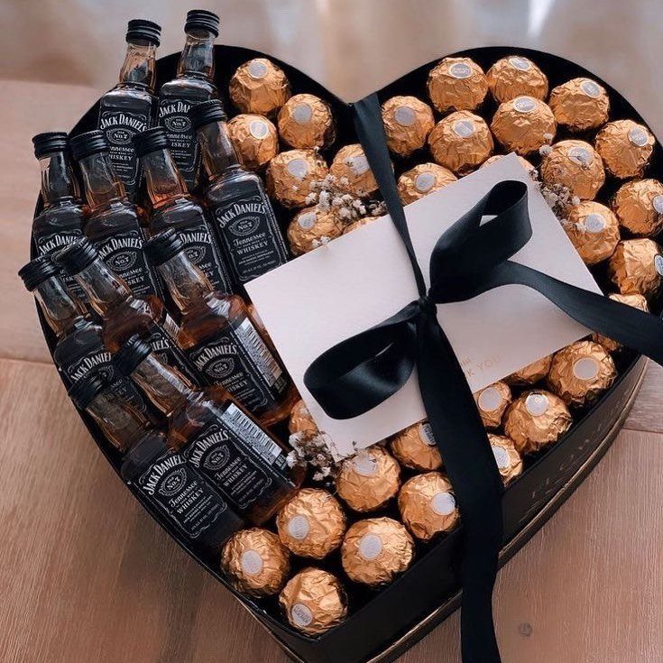 Heart-shaped gift box containing miniature whiskey bottles, gold chocolates, and a ribboned card.