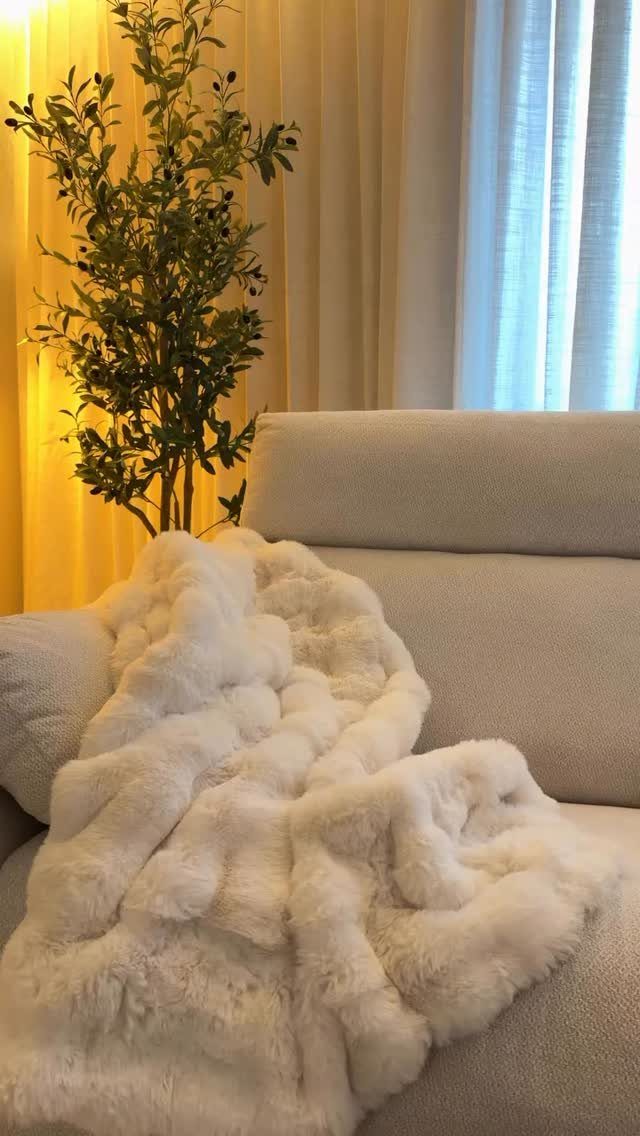 White faux-fur throw blanket draped over a light grey sofa next to a plant