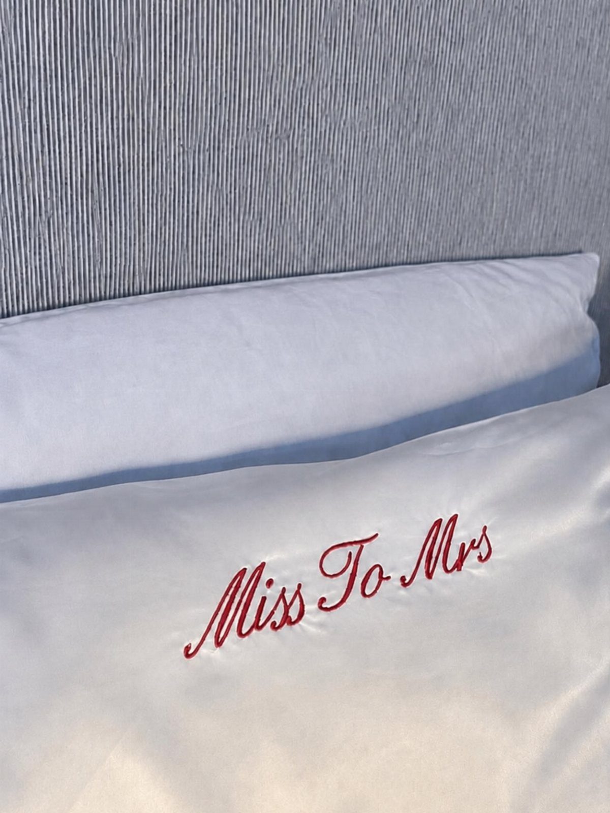 White satin robe with red Miss To Mrs embroidery on white bed linens.