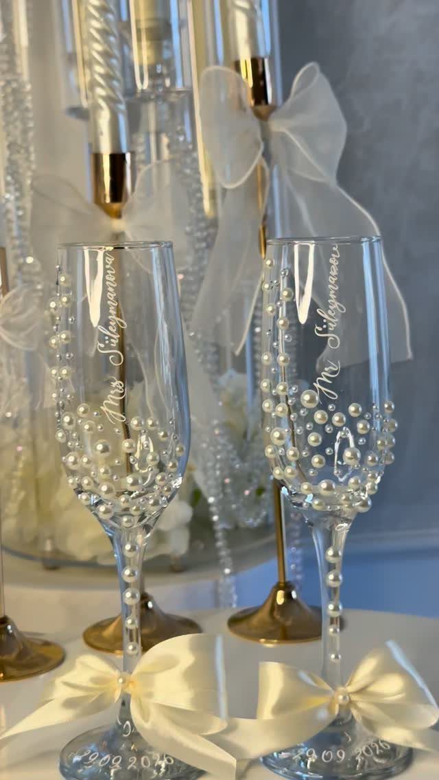 Two engraved champagne flutes decorated with white pearls and satin bows.