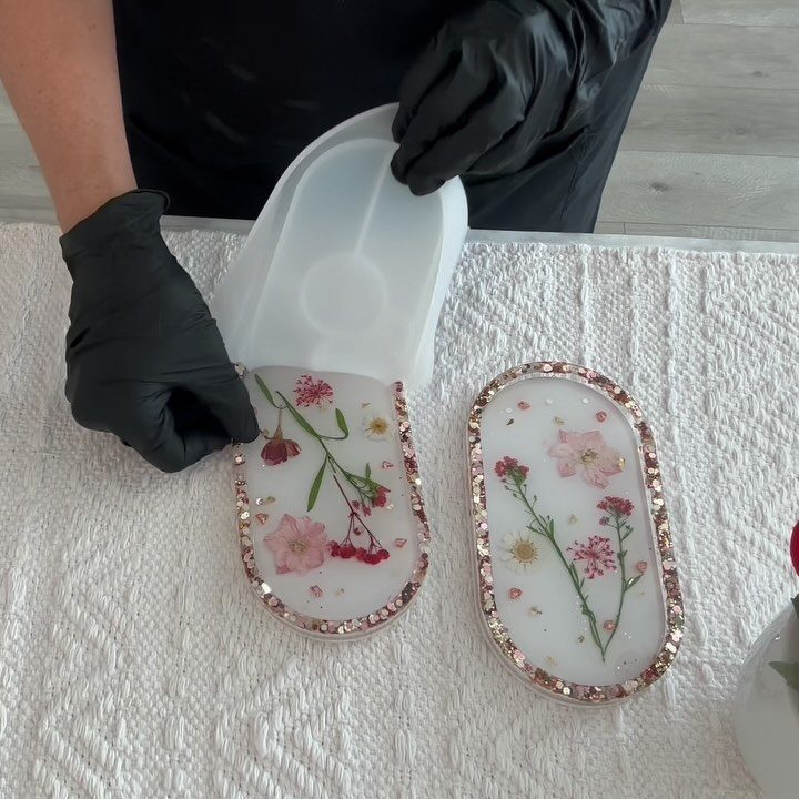 Resin trays with pressed flowers and gold glitter being removed from molds.