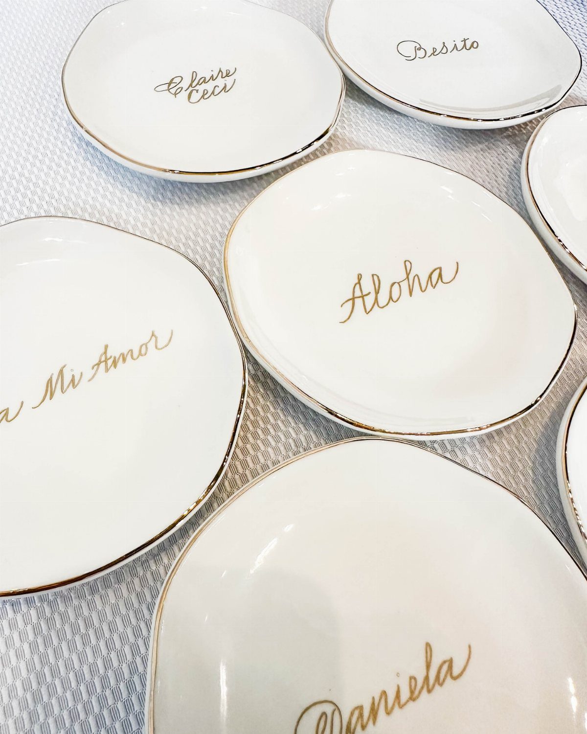 Small white ceramic jewelry dishes with gold rims and personalized gold cursive lettering.
