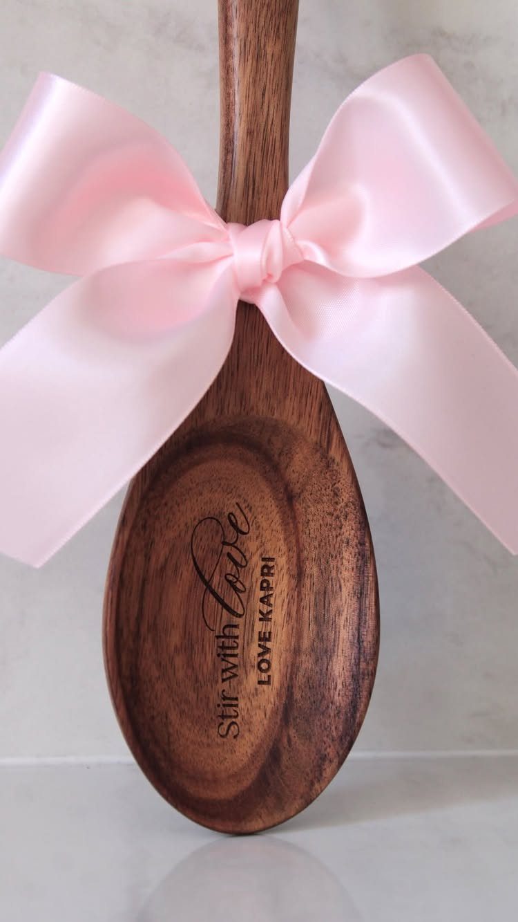 Engraved wooden spoon tied with a pink satin bow on white marble surface