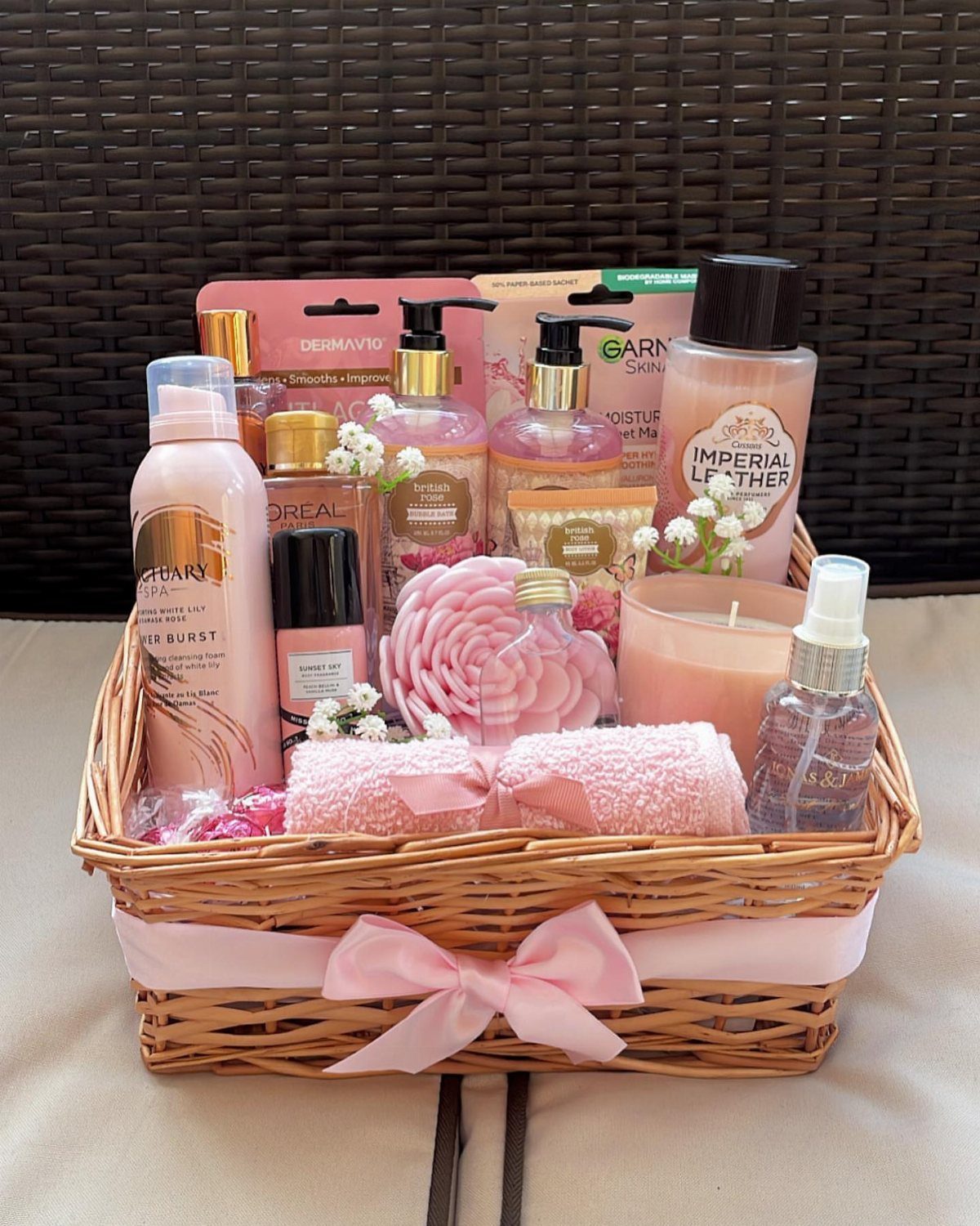 Wicker gift basket filled with pink beauty products, towels, and a pink ribbon.