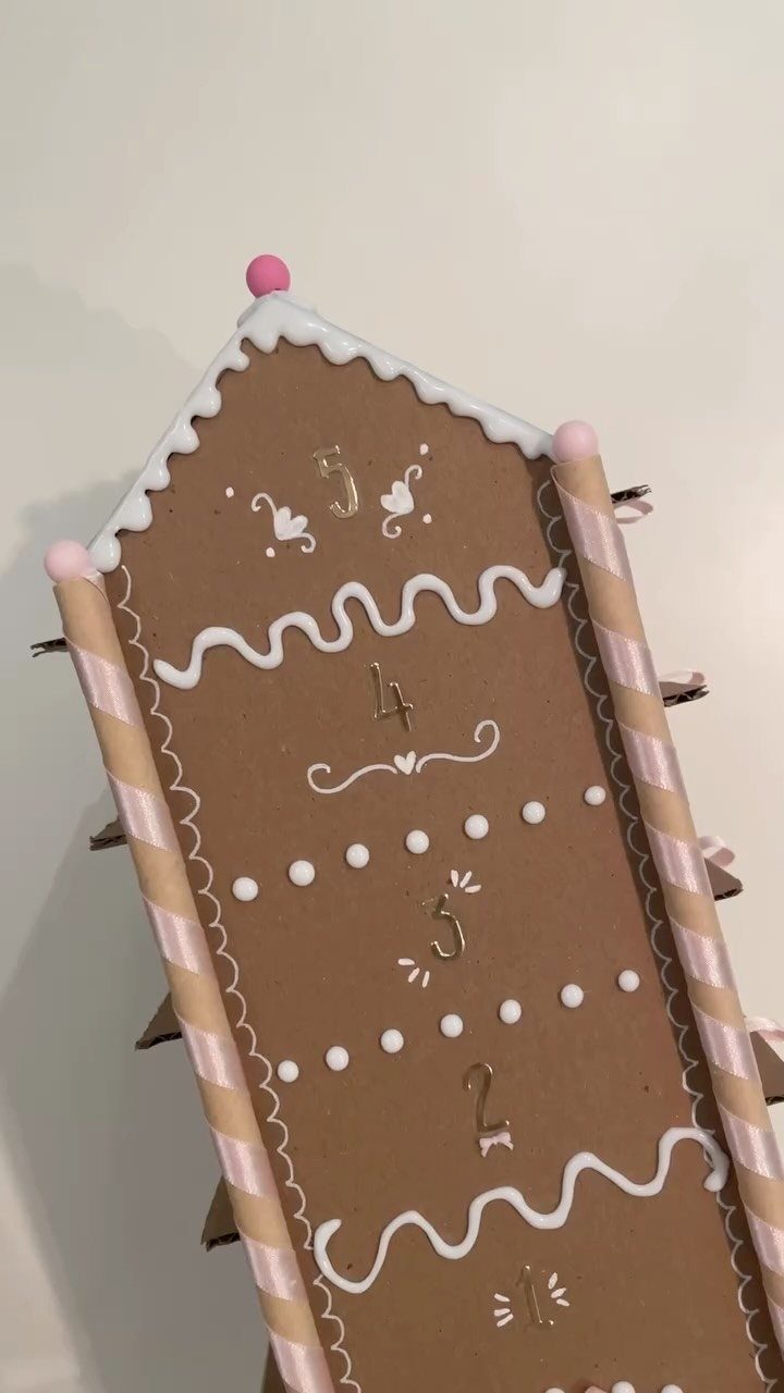 Cardboard house decorated like a gingerbread house with white paint and striped straws.