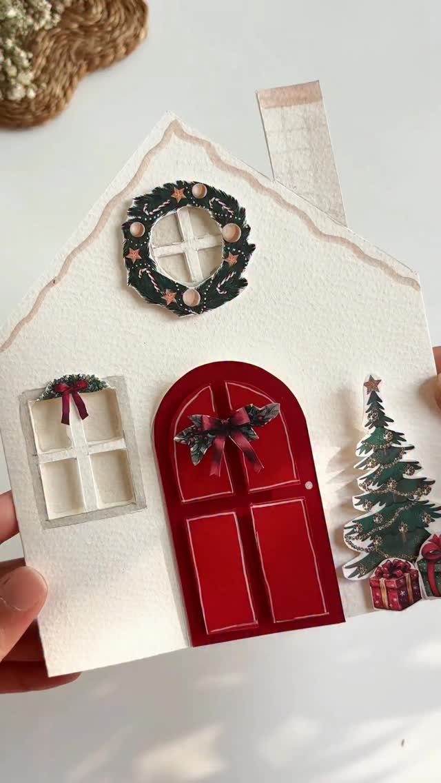 Handmade white paper house card with a red door and Christmas decorations.