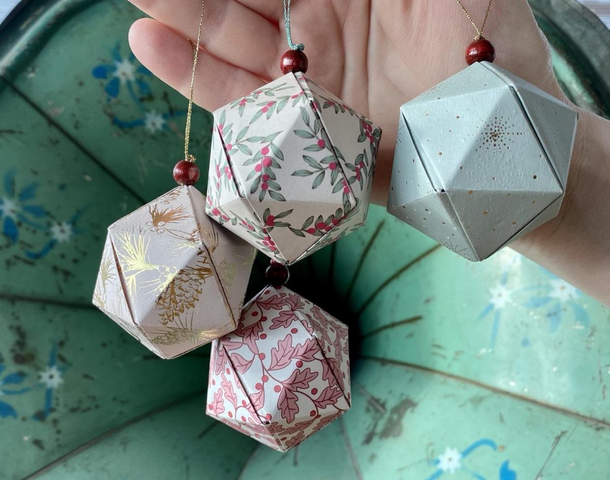 Four geometric paper ornaments with floral and gold patterns held in a hand.