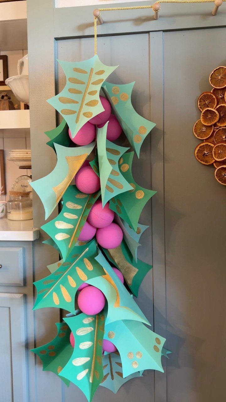 Teal paper holly leaves and pink paper spheres forming a vertical Christmas garland.