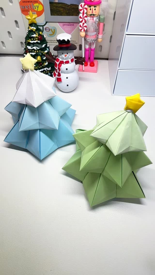 Two origami Christmas trees made of blue and green paper with yellow stars.