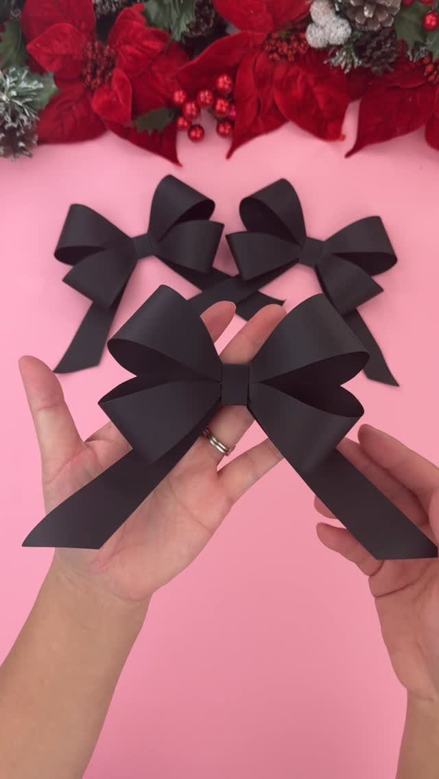 Black paper bows held by hands against a pink background with red poinsettias.