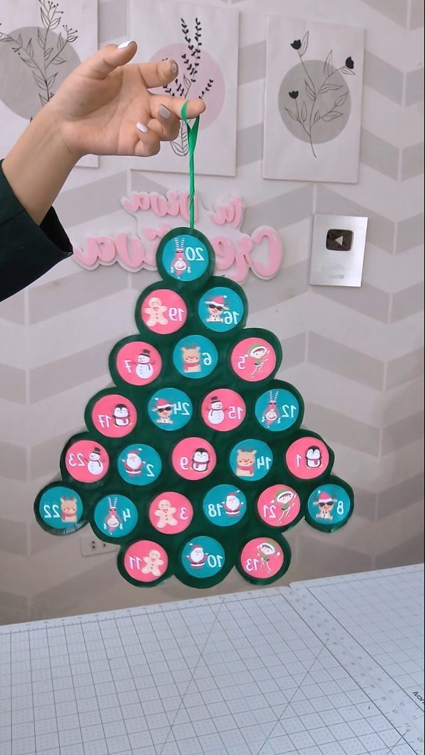 Paper Christmas tree advent calendar with numbered circular flaps held by a hand.