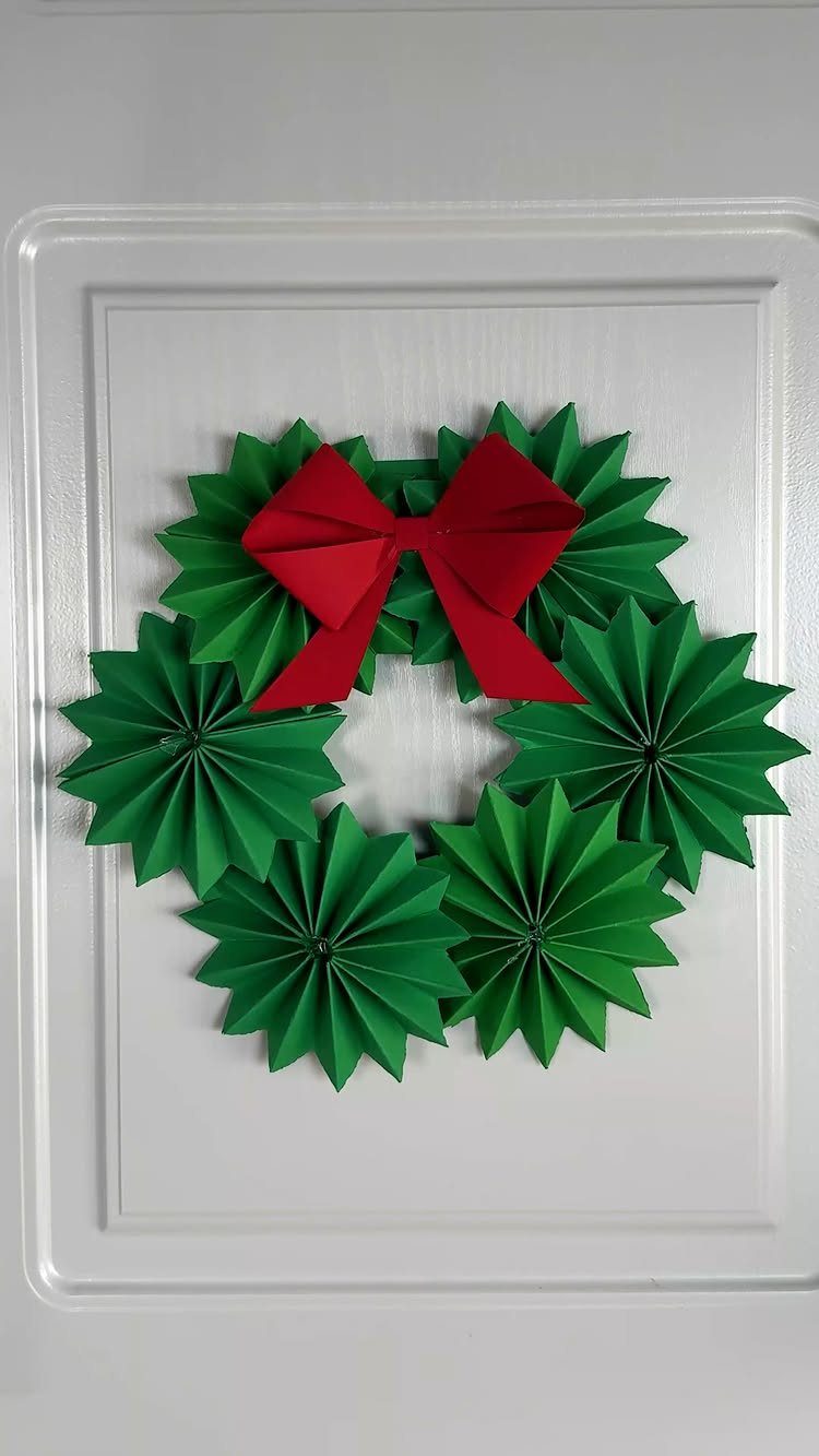 Green pleated paper fan wreath with a red bow on a white door