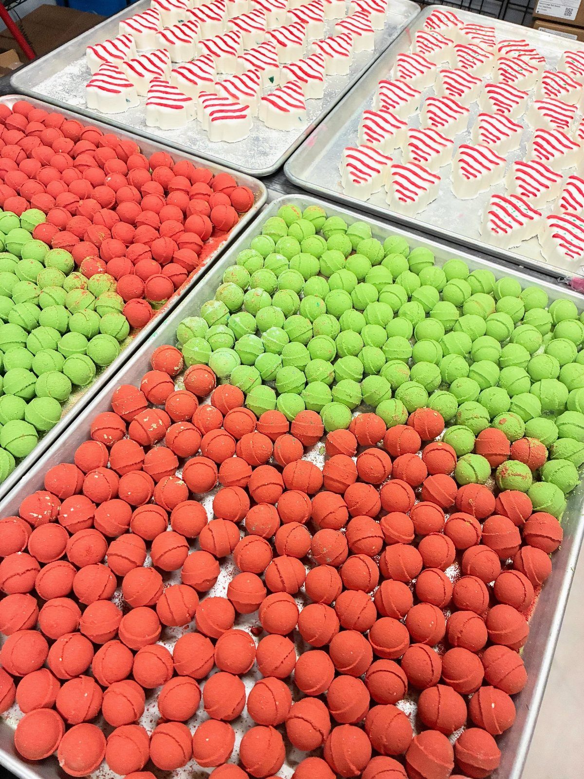 Red and green spherical bath bombs and striped white ones on metal trays.