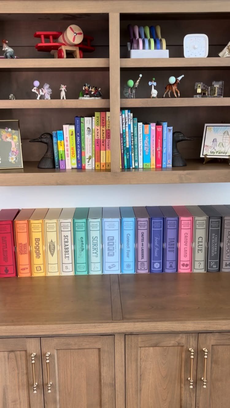Rainbow colored board game boxes arranged on a wooden shelf in a home.