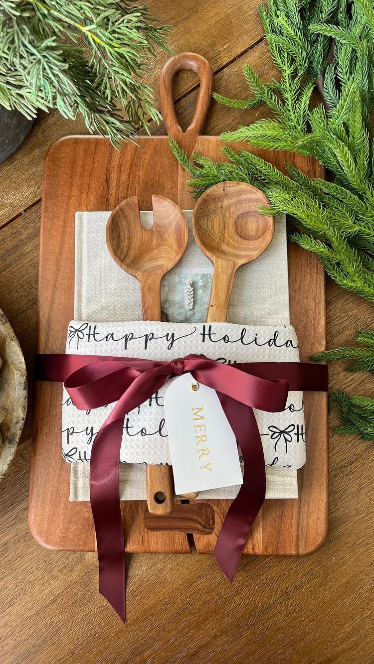 Wooden cutting board gift set with serving spoons, holiday towels, and burgundy ribbon.