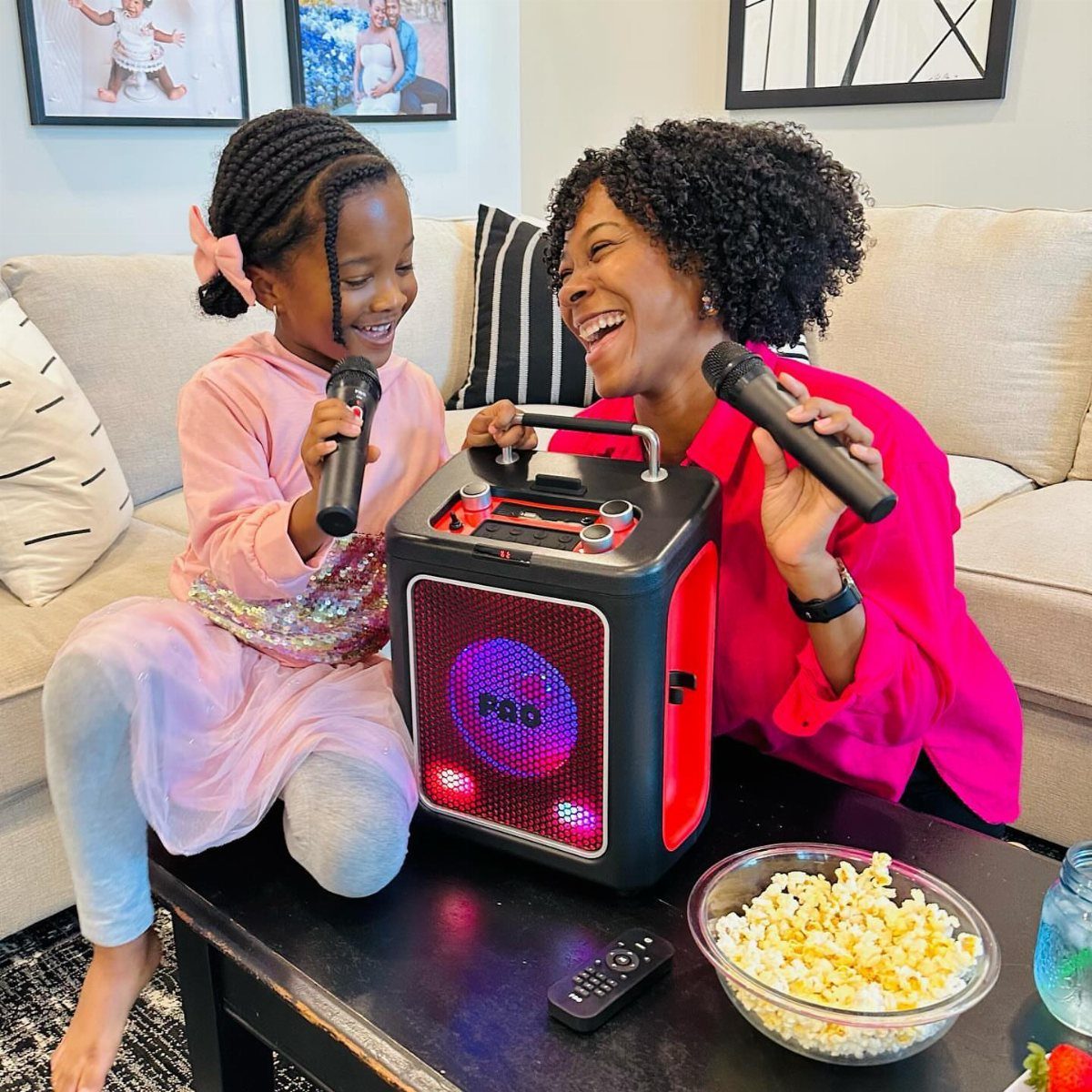 Woman and young girl singing into microphones with a portable karaoke machine and popcorn.