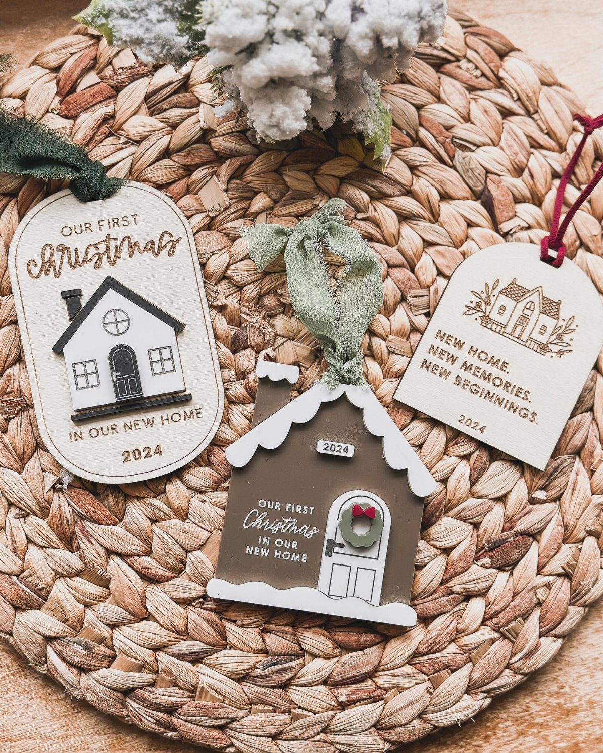 Three personalized house-shaped Christmas ornaments celebrating a first home on a woven mat.