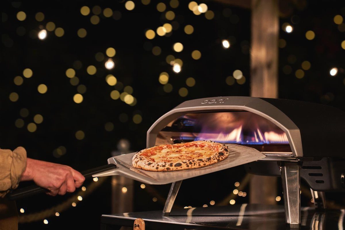 Pizza being removed from a portable outdoor pizza oven with a metal peel