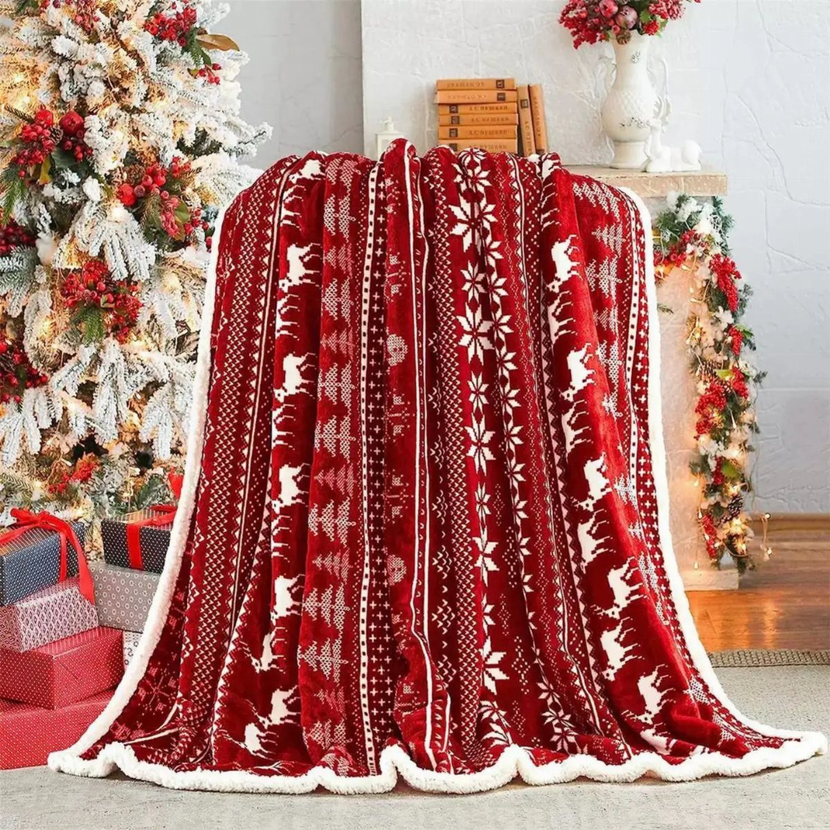Red plush Christmas blanket with white reindeer patterns draped near a decorated tree.
