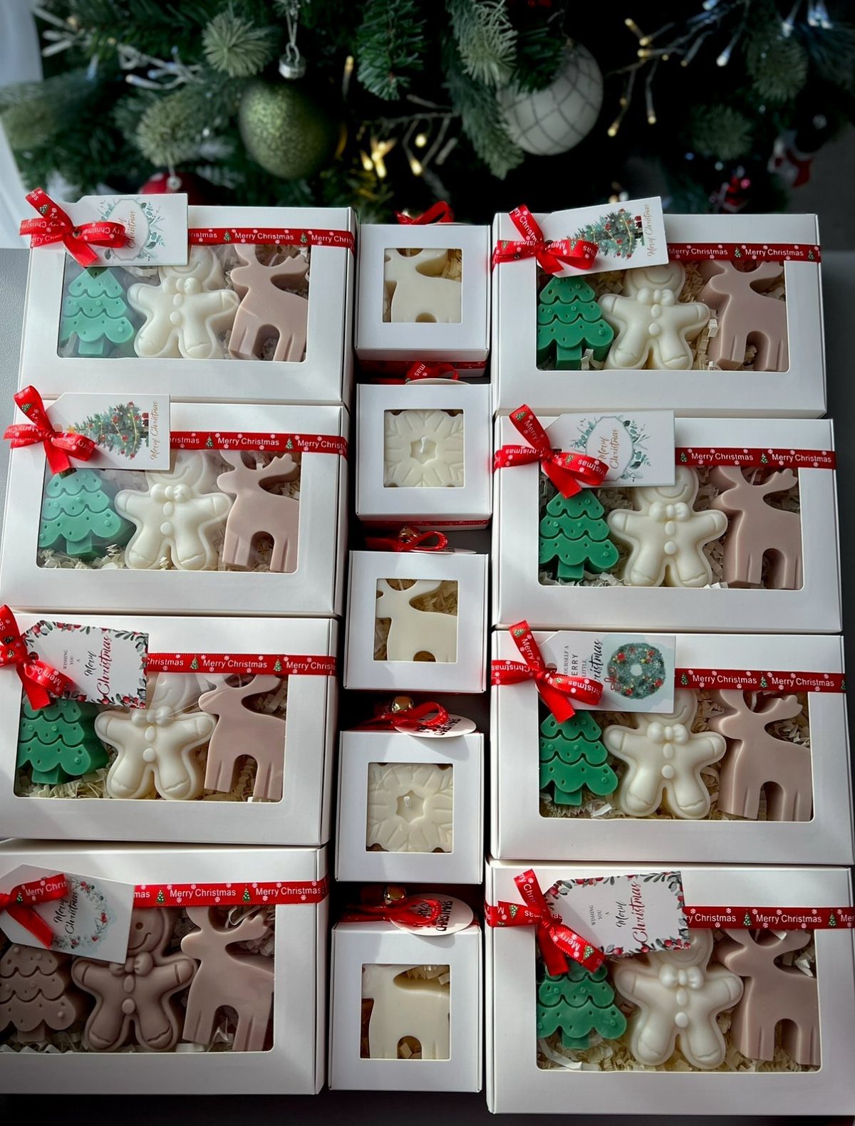 Christmas shaped candles in white gift boxes with red ribbons and tags.